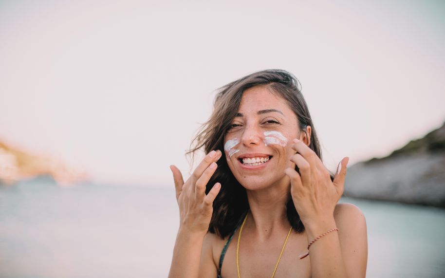 Uso de protector solar en personas con psoriasis durante el verano Mujer joven con psoriasis aplicándose sonriente protector solar